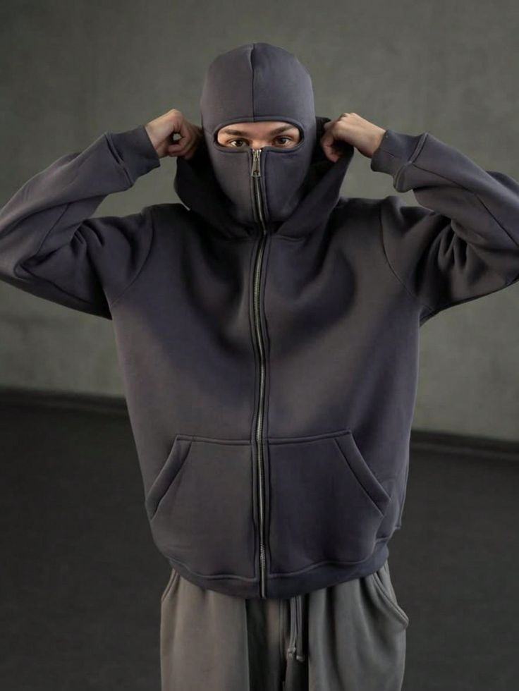 Person wearing a dark gray hoodie with a face mask over a plain background