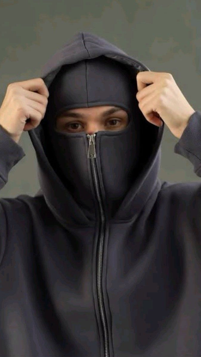 Person wearing a dark gray hoodie with a zipper, adjusting the hood against a neutral background.