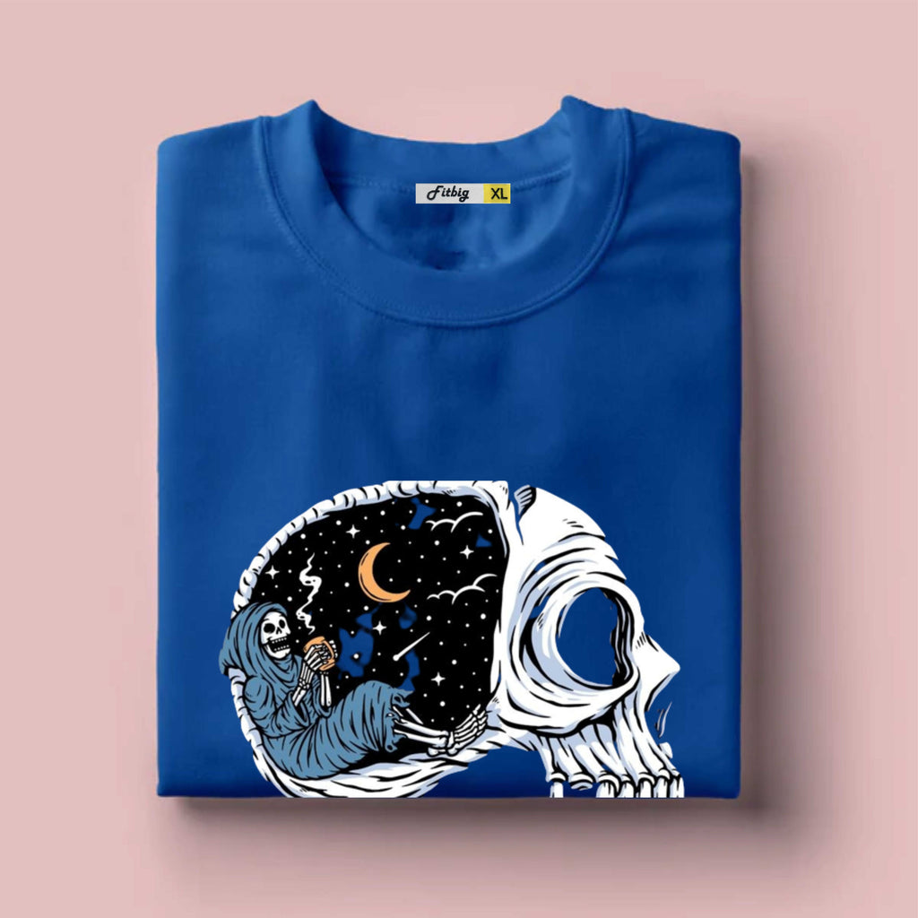 Folded blue t shirt with a skull design featuring a crescent moon and stars on a pink background